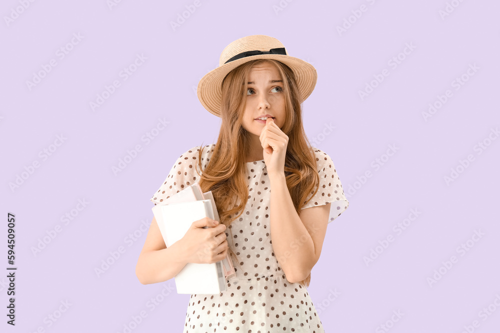 Young woman with books biting nails on lilac background