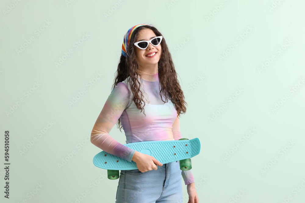 Teenage girl in sunglasses with skateboard on green background