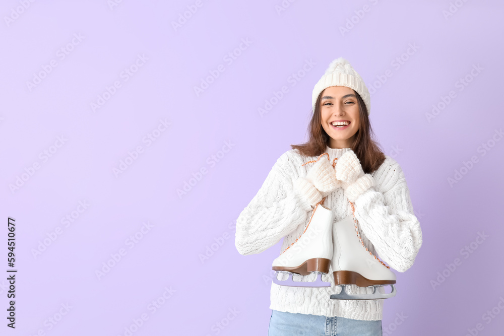 Pretty young woman with ice skates on lilac background