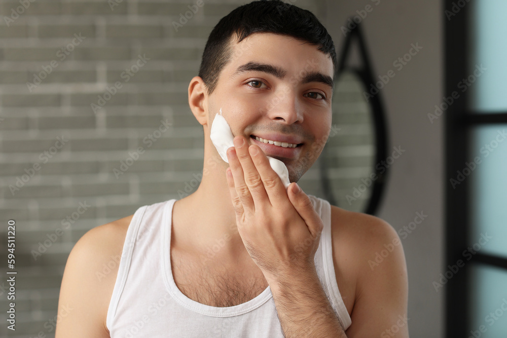 Young man applying shaving foam onto face in bathroom