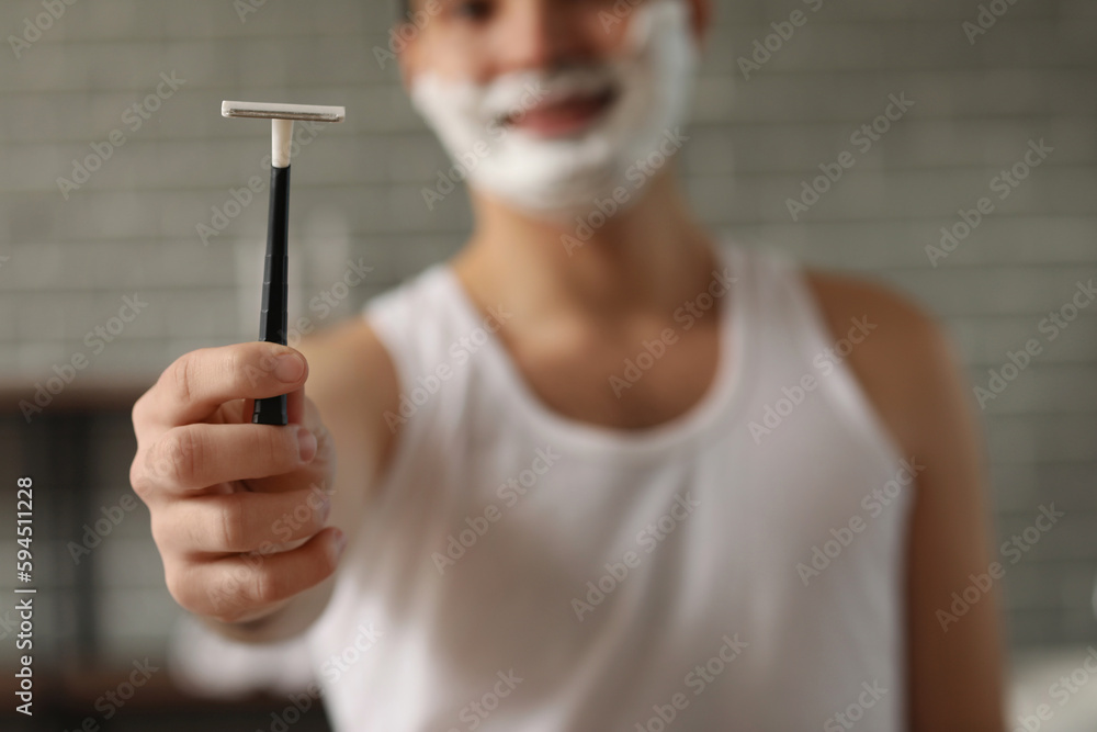 Young man with razor in bathroom, closeup