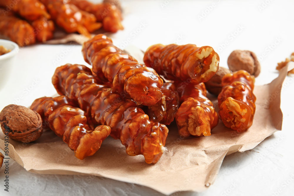 Paper sheet with tasty churchkhela and walnuts on light table, closeup