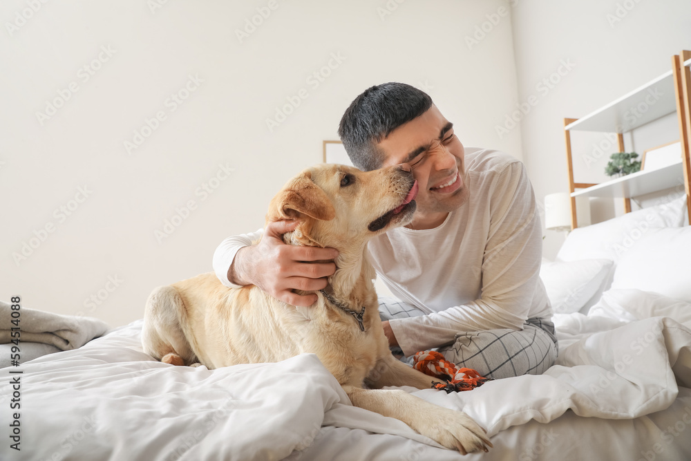 Young man with cute Labrador dog and toy sitting in bedroom