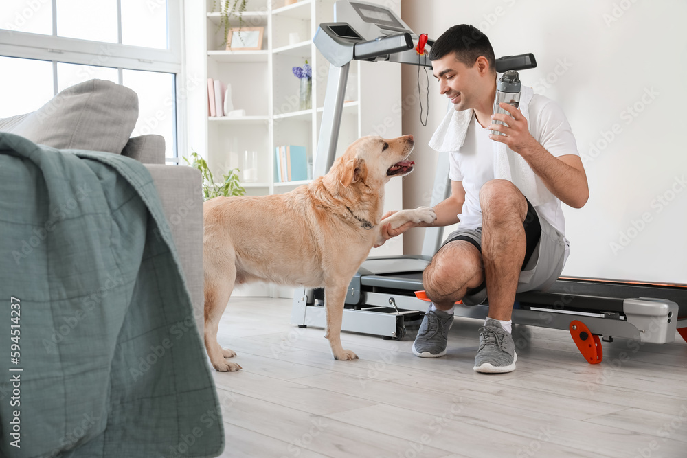 Sporty young man with bottle of water and cute Labrador dog at home