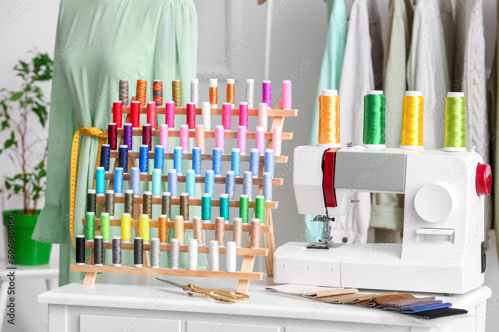 Stand with thread spools and sewing machine on table in atelier