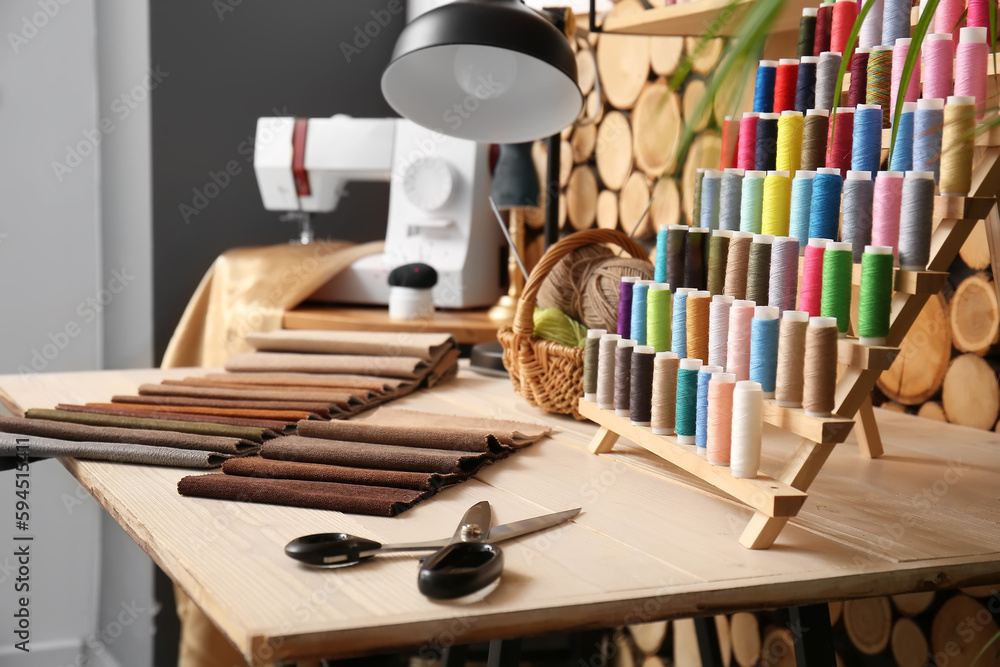 Stand with thread spools, scissors and fabric samples on table in atelier, closeup