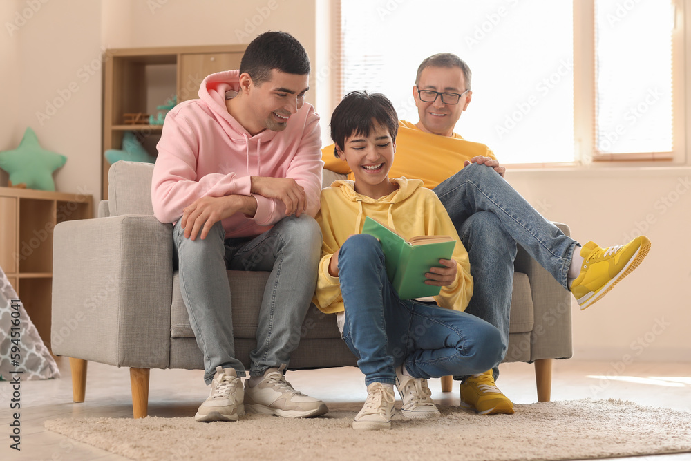 Happy little boy with his dad and grandfather reading book at home