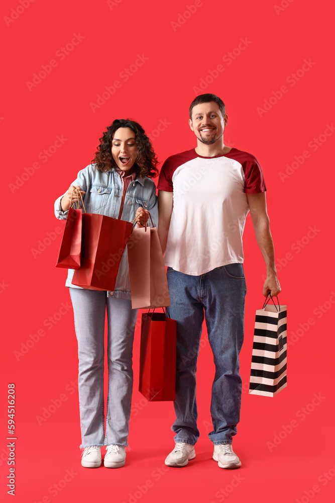 Young couple with shopping bags on red background