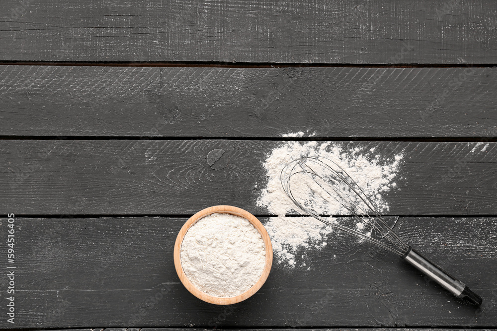 Bowl with wheat flour and whisk on black wooden table