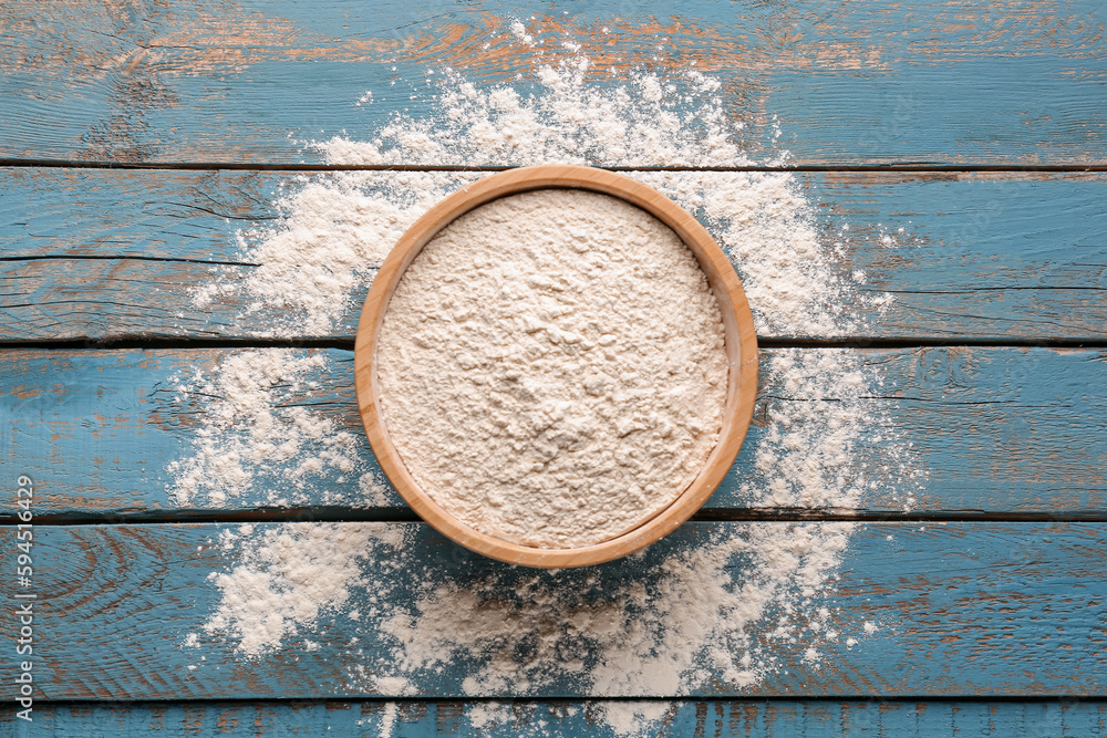 Bowl with wheat flour on blue wooden table