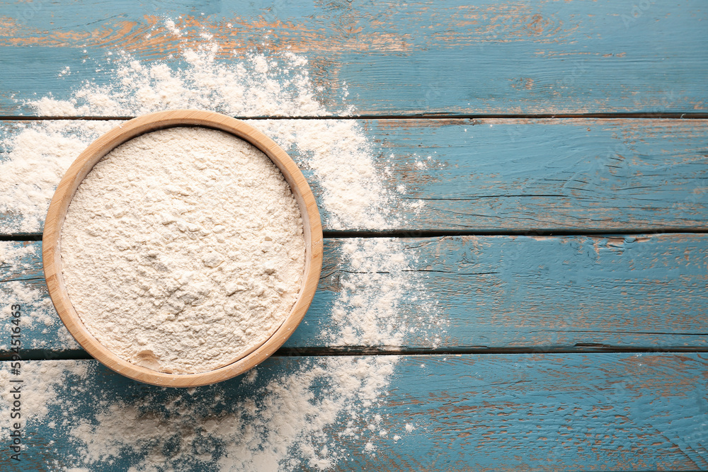 Bowl with wheat flour on blue wooden table