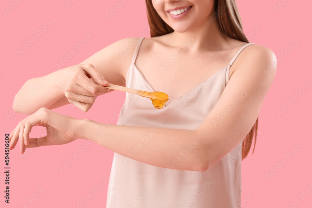 Young woman applying sugaring paste onto her arm against pink background