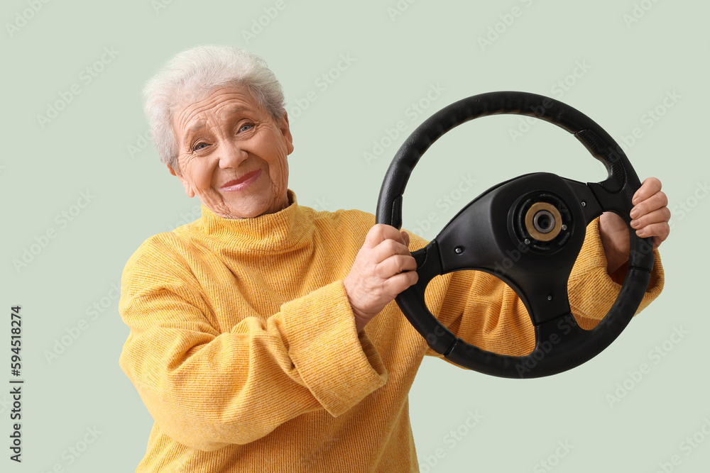 Senior woman with steering wheel on green background