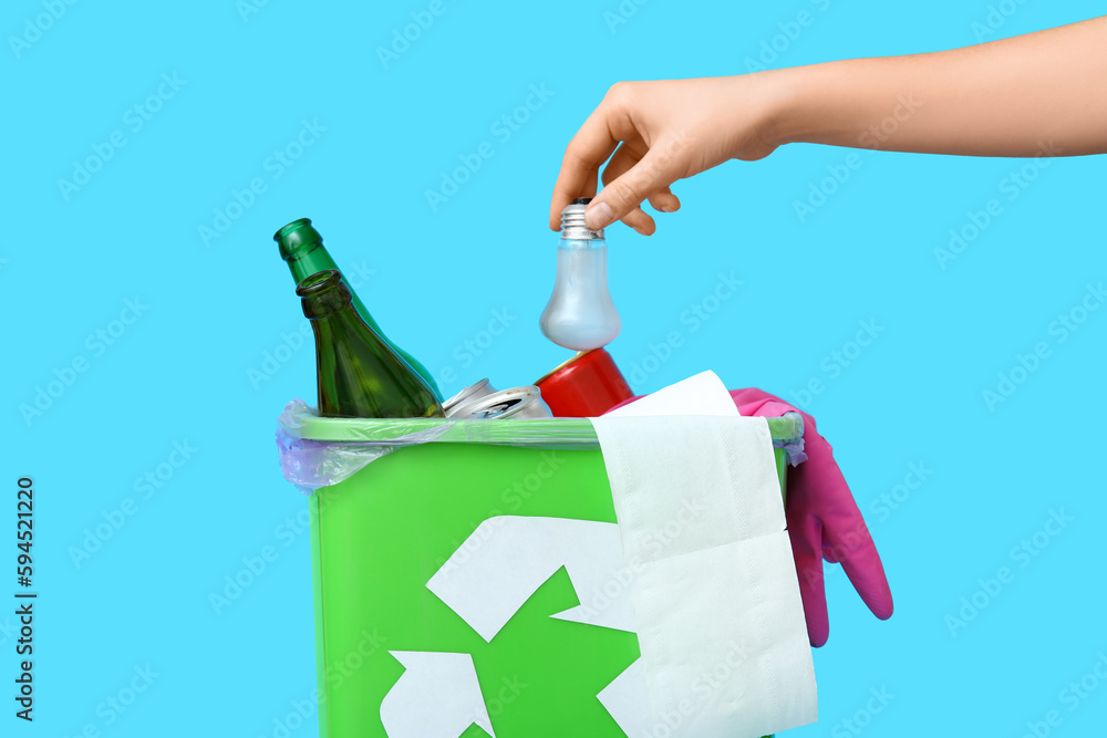 Woman throwing garbage into trash bin on blue background, closeup