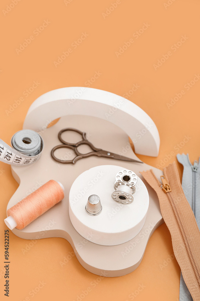 Podiums with tailors supplies on orange background