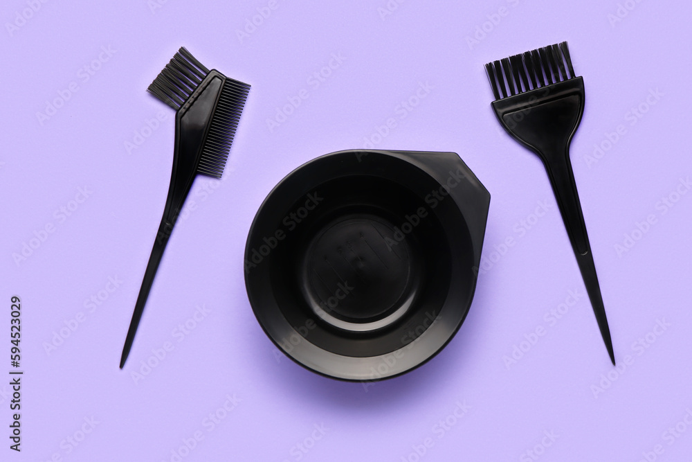 Hairdressers brushes with bowl on violet background