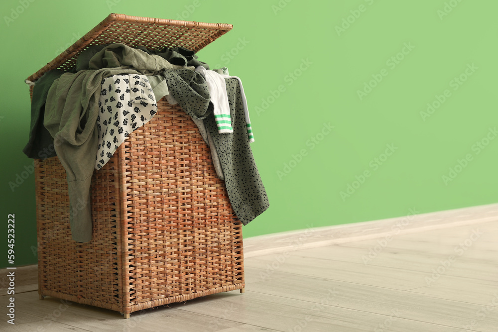 Wicker basket with dirty clothes near green wall