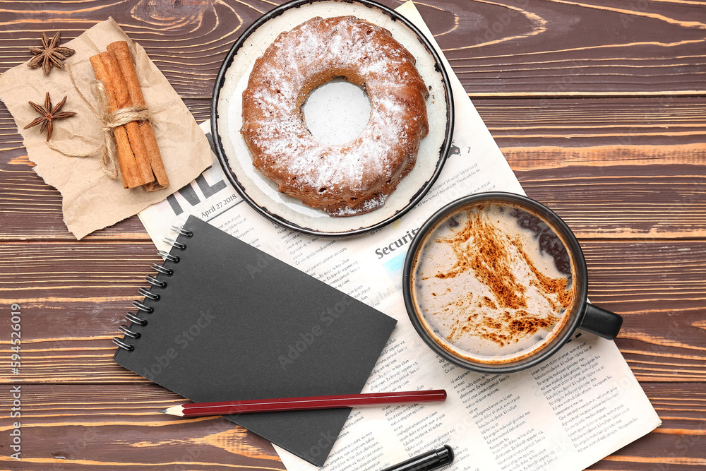 Cup of coffee with cake, cinnamon, notebook and newspaper on wooden background