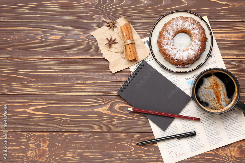 Cup of coffee with cake, cinnamon, notebook and newspaper on wooden background