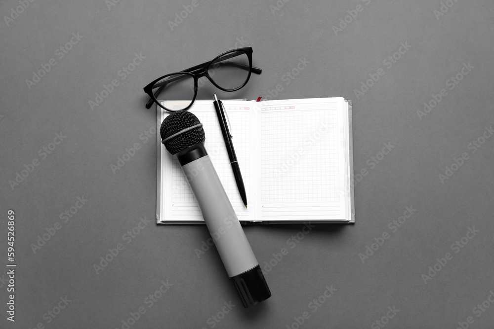 Notebook with pen, microphone and eyeglasses on dark background