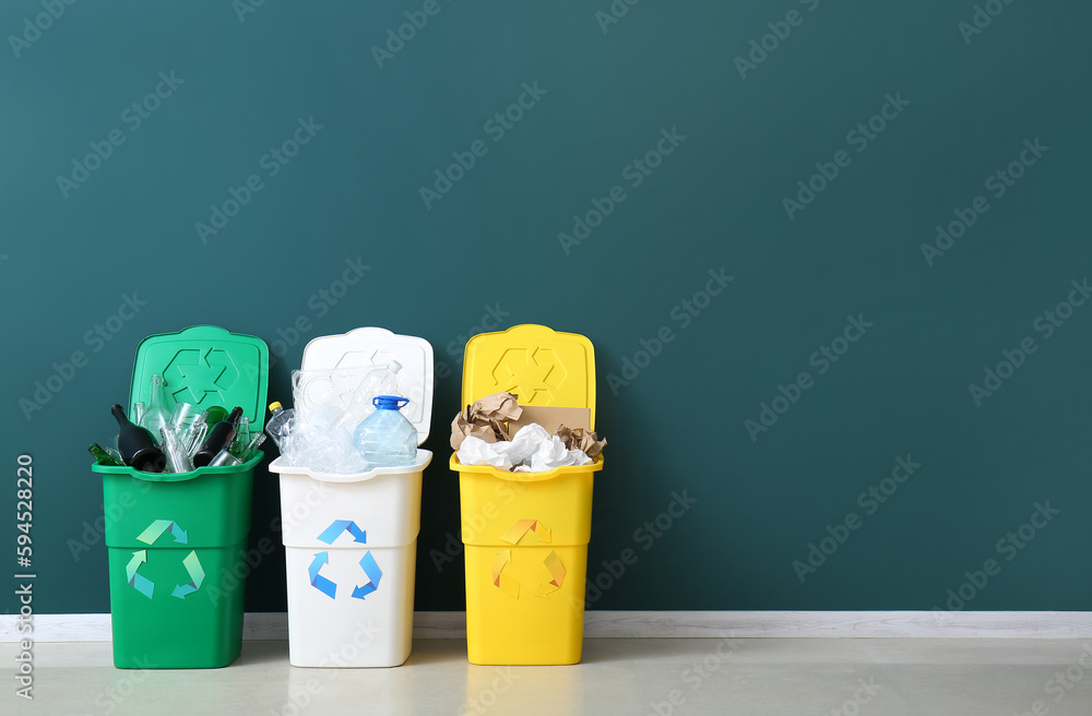 Trash bins with recycling symbol and different garbage near green wall