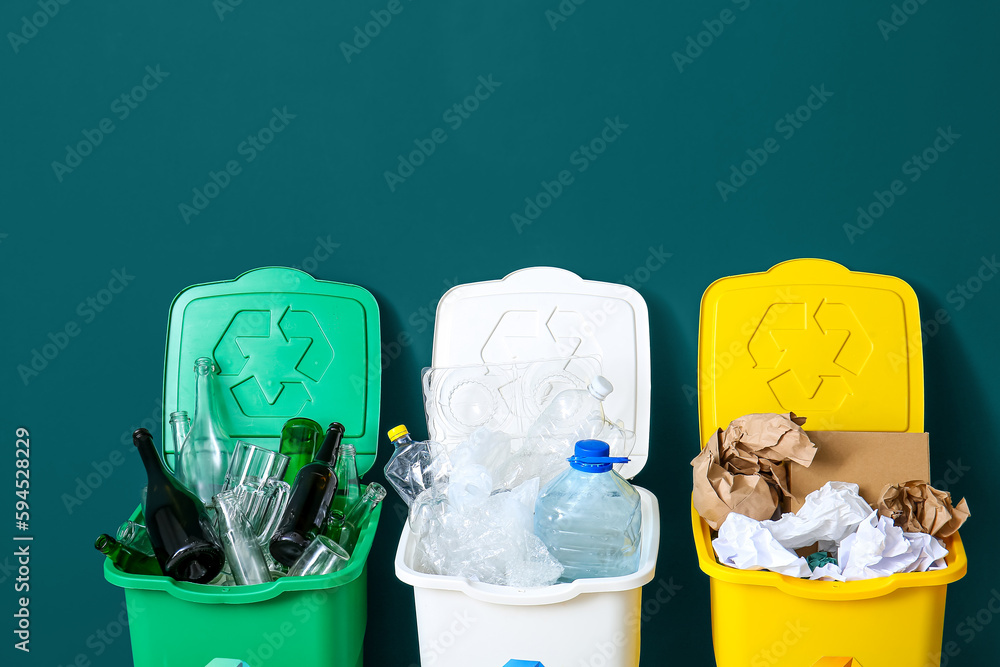 Trash bins with recycling symbol and different garbage near green wall