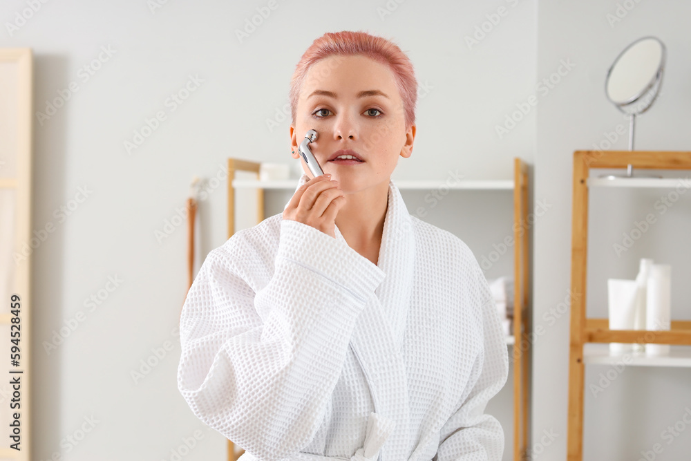 Young woman with facial massage tool in bathroom