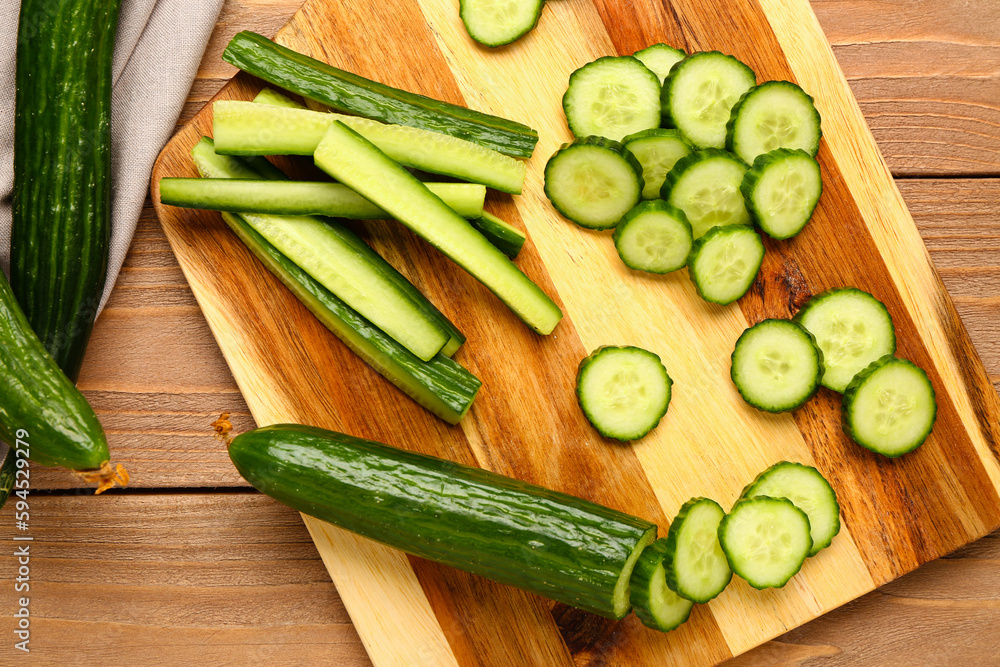 Board with cut cucumber on wooden background