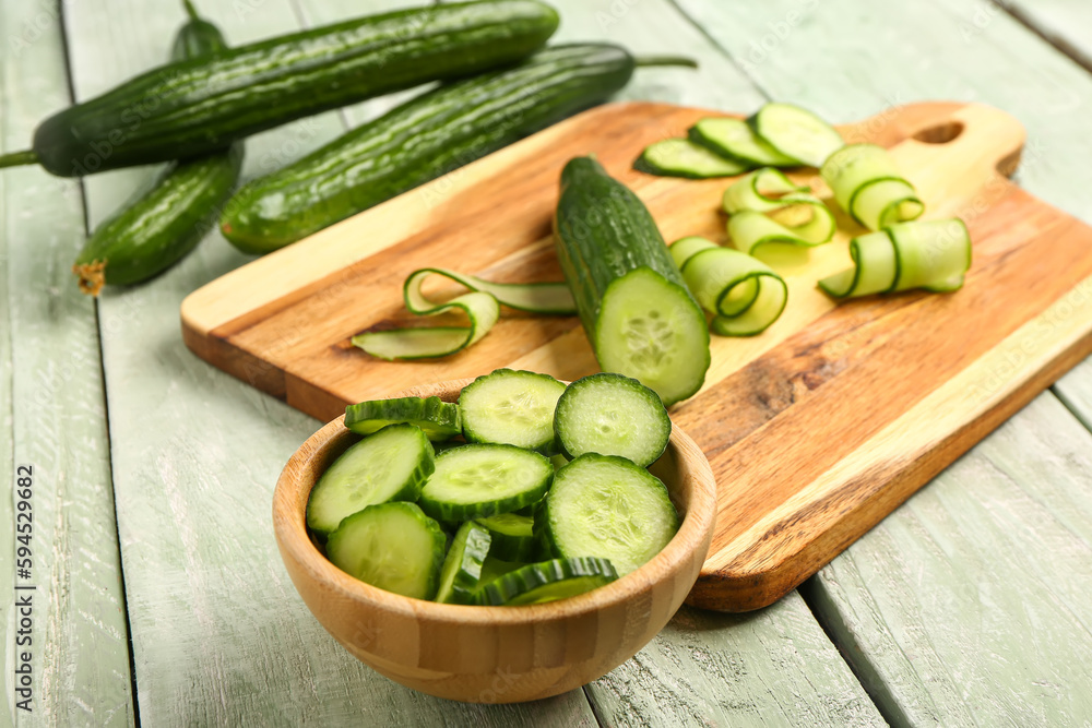 Bowl with fresh cut cucumber on light wooden background