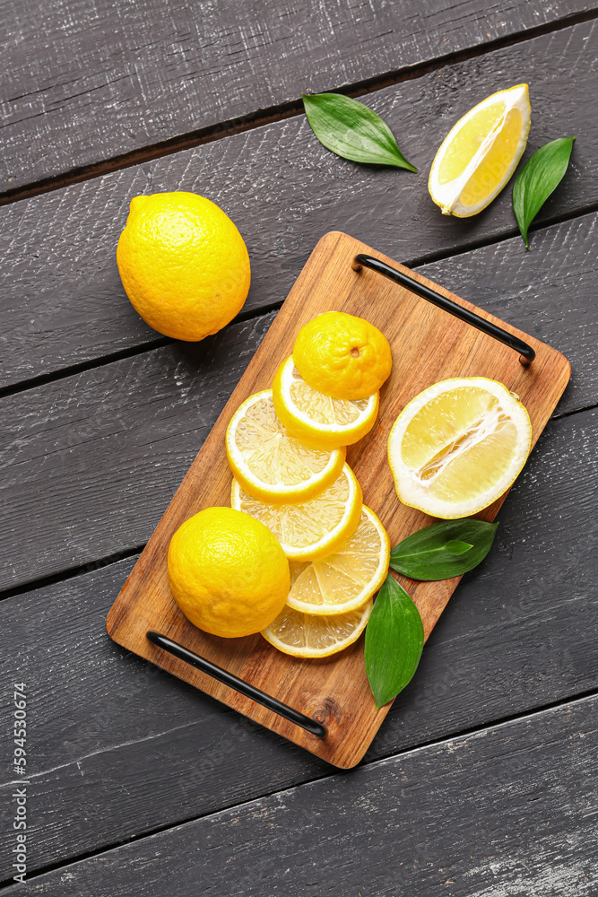 Board with fresh lemons on black wooden background