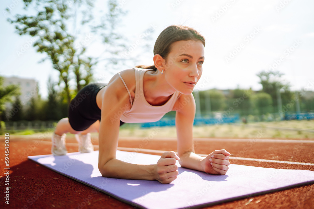 Sportswoman doing exercises outdoors in the morning. Energetic woman doing exercises on the sports g