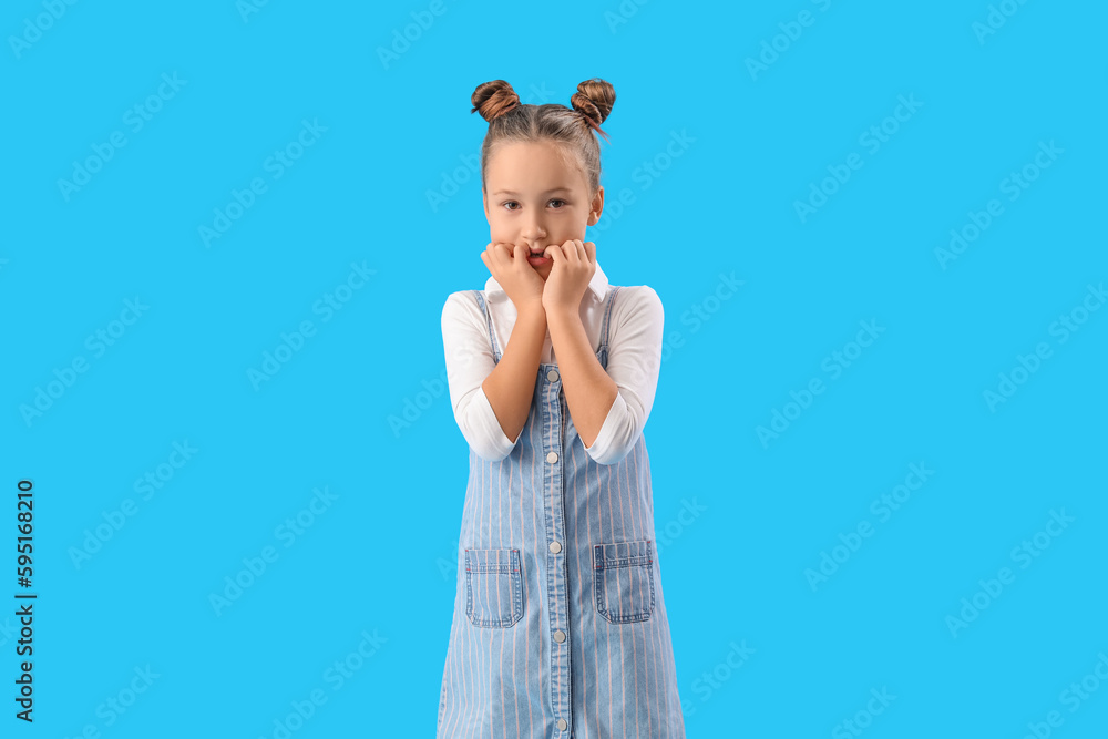 Little girl biting nails on blue background