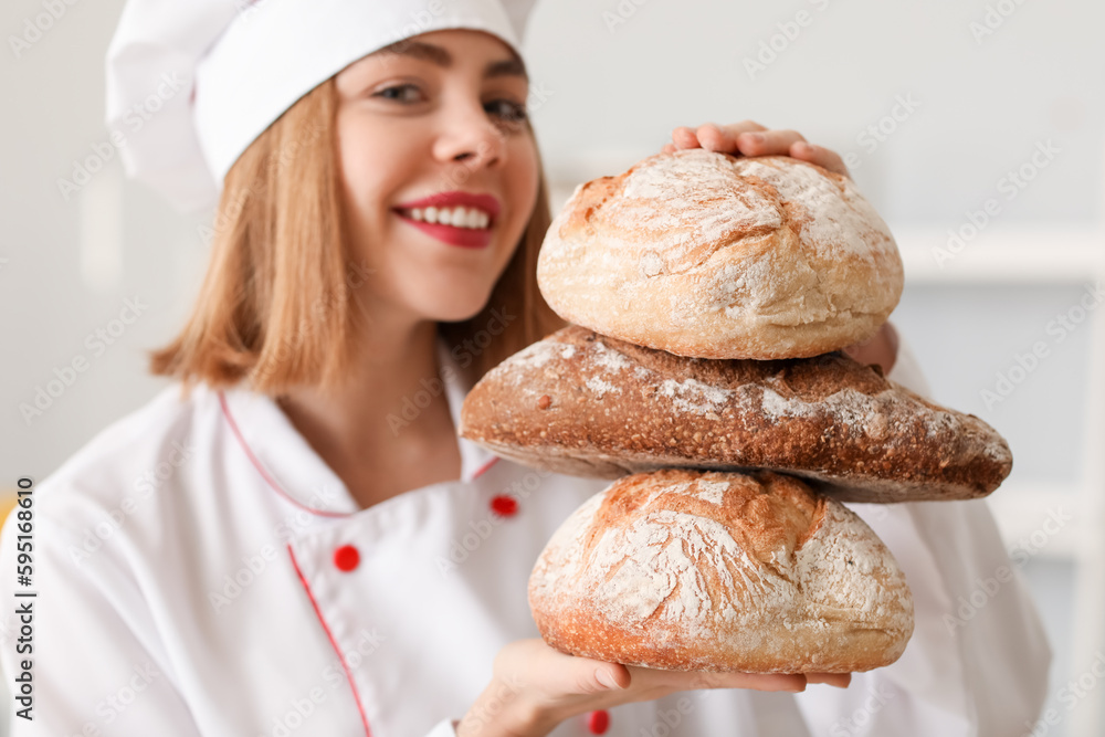 Female baker with loaves of fresh bread in kitchen, closeup