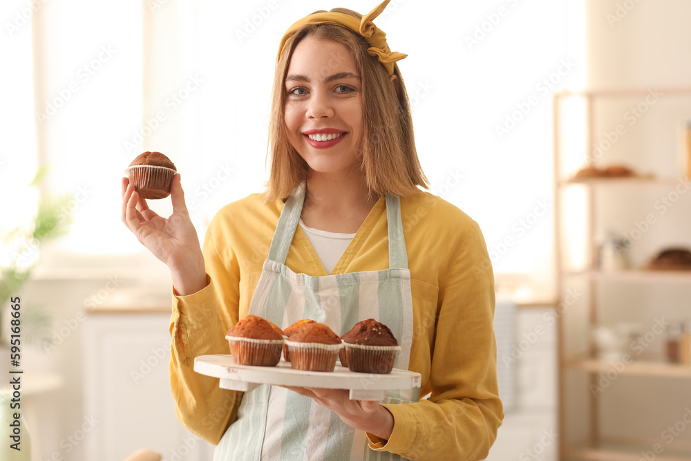 Female baker with tray of tasty cupcakes in kitchen