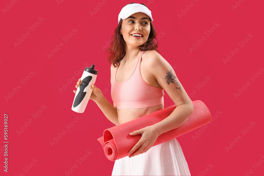 Sporty young woman with bottle of water and mat on pink background