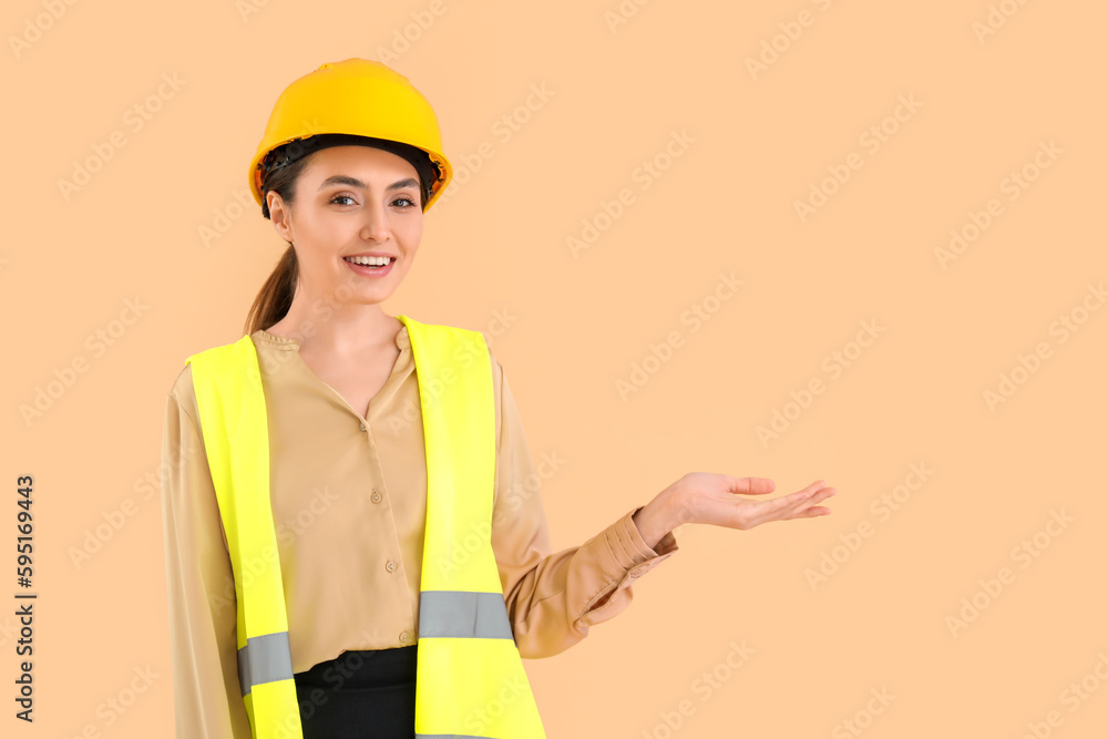 Female worker in vest and hardhat showing something on beige background