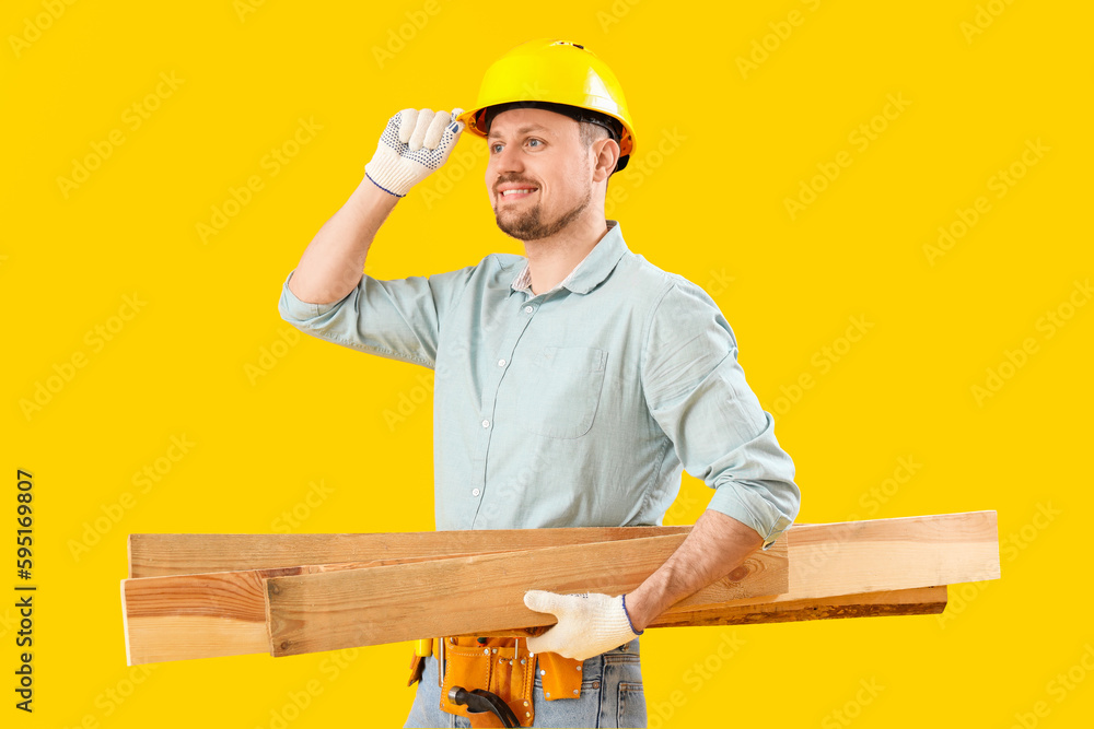 Male carpenter with wooden planks on yellow background