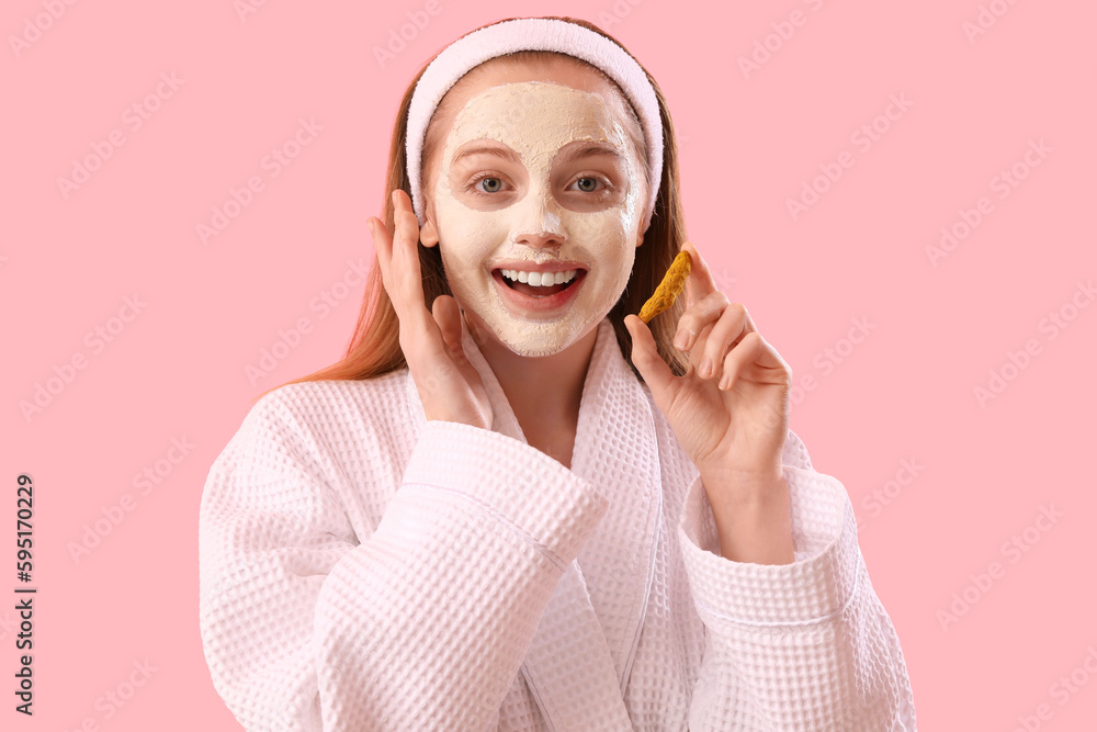 Surprised young woman with applied turmeric mask and root on pink background