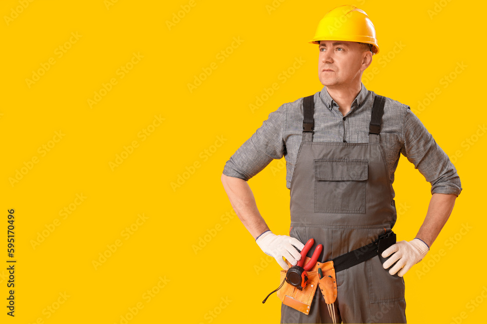 Mature carpenter in hardhat on yellow background