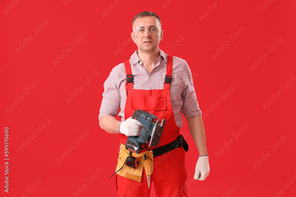 Mature carpenter with cordless jigsaw on red background