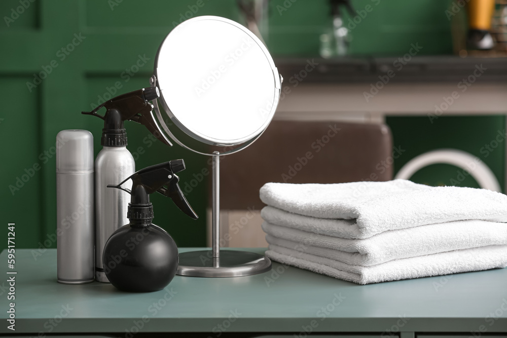 Different hair sprays, towels and mirror on table in beauty salon