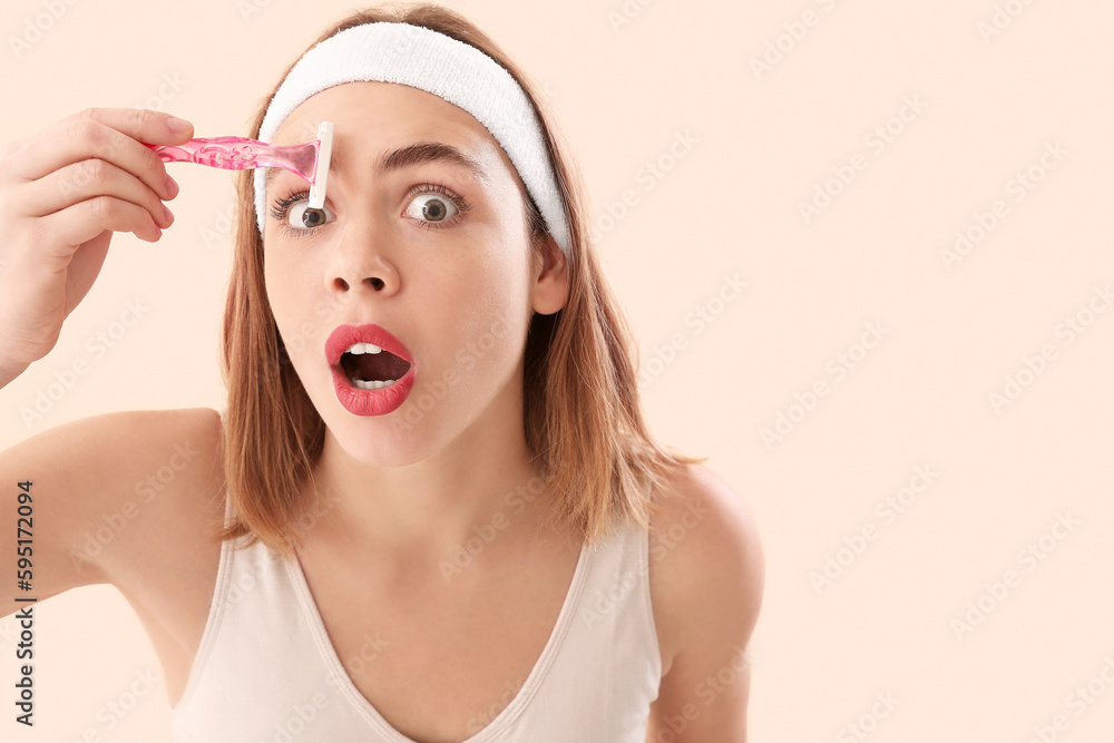 Shocked young woman shaving her brow with razor on beige background, closeup