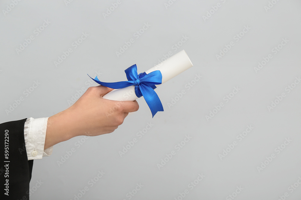 Woman holding diploma with ribbon on grey background