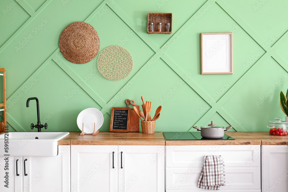 White kitchen counters with sink and utensils near green wall