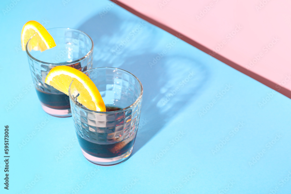 Glasses of rum with ice cubes and lemon slices on colorful background