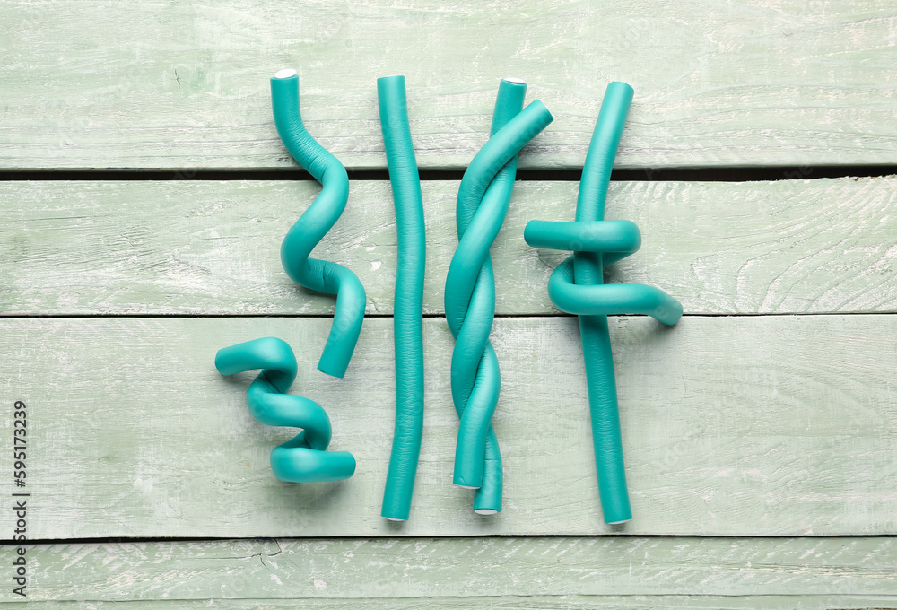 Hair curlers on green wooden background