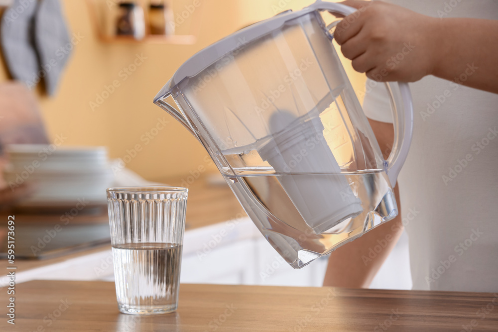 Man pouring water from filter jug into glass on table in kitchen