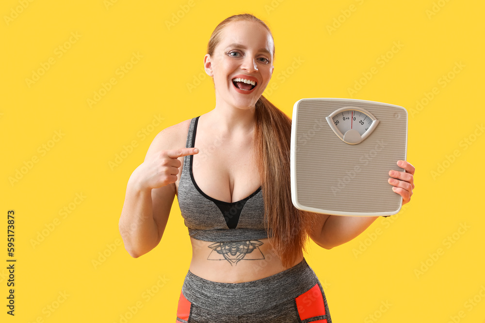 Young overweight woman pointing at scales on yellow background