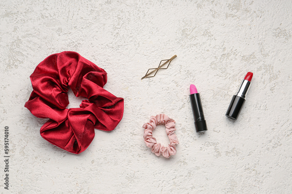 Silk scrunchies, hairpin and lipsticks on light background