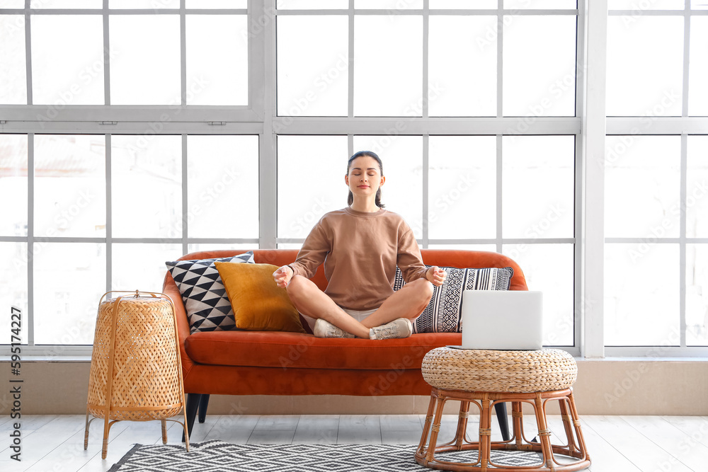 Beautiful woman meditating on sofa at home